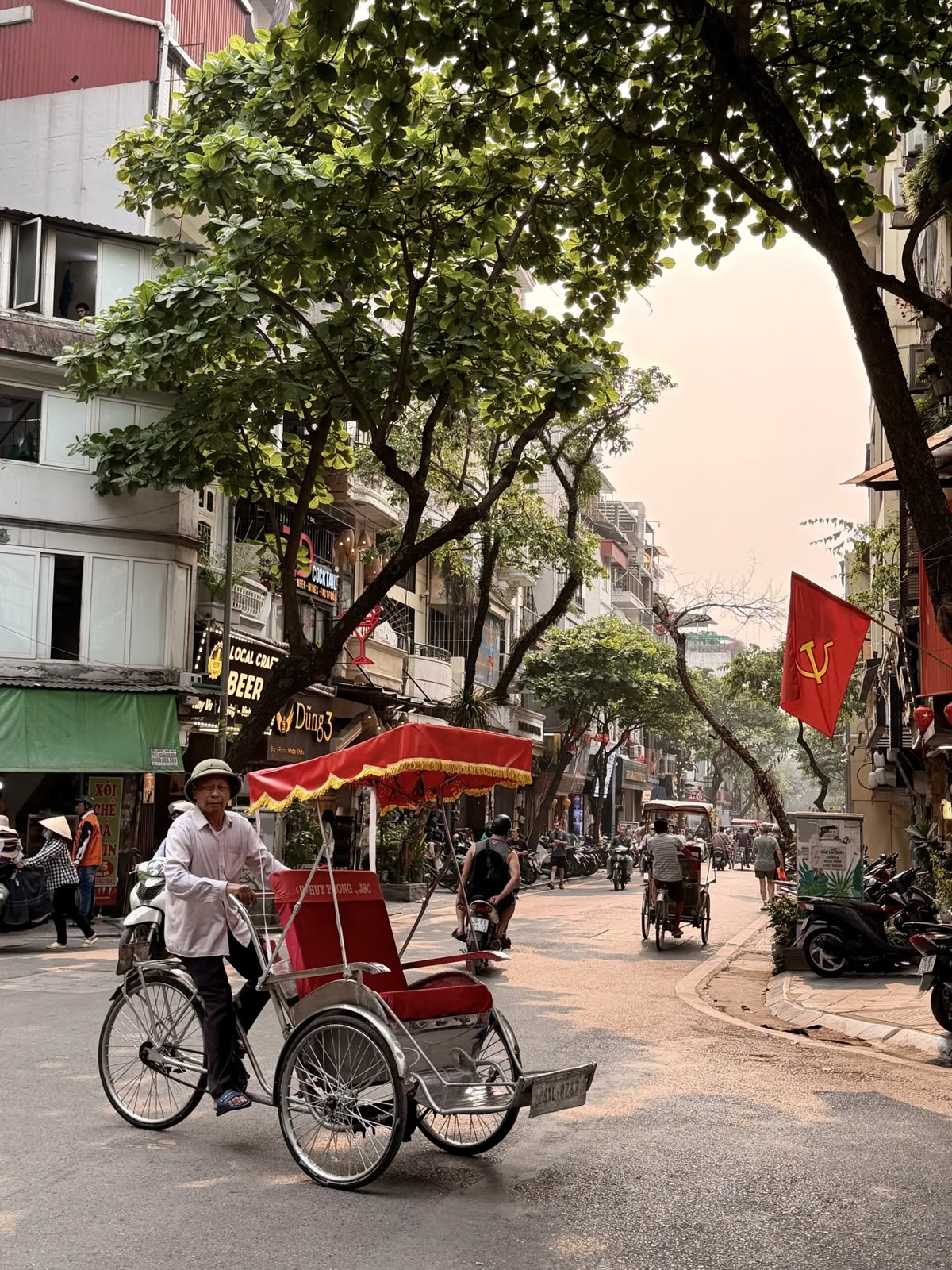 Morning sunlight illuminating the traditional street life and cyclos of the Hanoi Old Quarter.